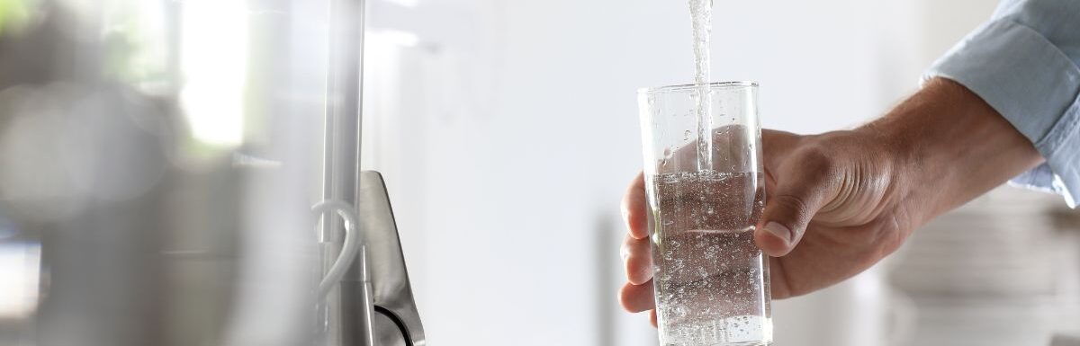 Man pouring water from the faucet into glass in the kitchen.