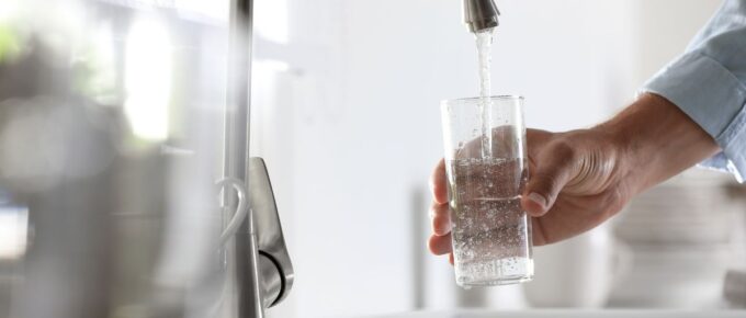 Man pouring water from the faucet into glass in the kitchen.