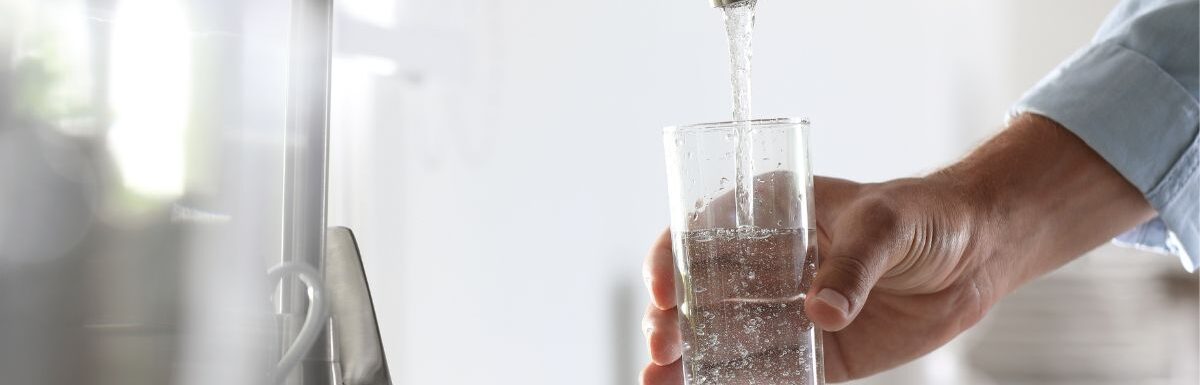 Man pouring water into glass in kitchen, closeup.