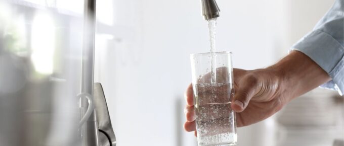 Man pouring water into glass in kitchen, closeup.