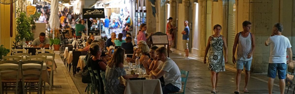 Tourists dining drinking and shopping in the evening on the streets of Kerkyra Old Town Corfu, Greece.