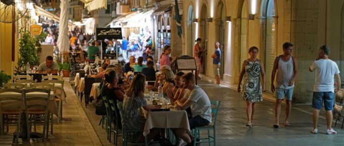 Tourists dining drinking and shopping in the evening on the streets of Kerkyra Old Town Corfu, Greece.