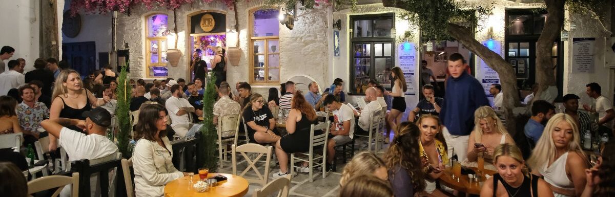 Young tourists surrounded by bars, enjoying drinks and cocktails at the popular square in Ios Greece at night.