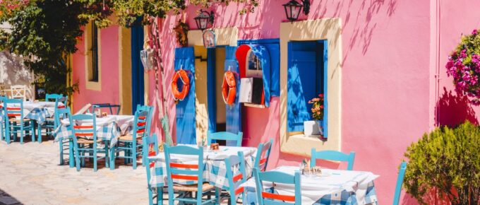 Traditional greek vivid lilac colored tavern on the narrow Mediterranean street on hot summer day.