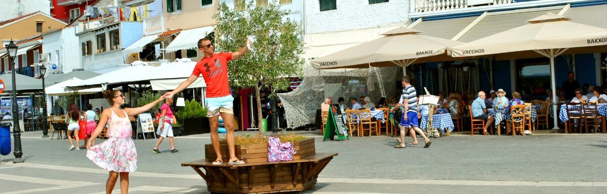 Paxos harbour with a young couple taking a selfie in the town centre while visiting the small island south of Corfu a Greek island in the Ionian sea.