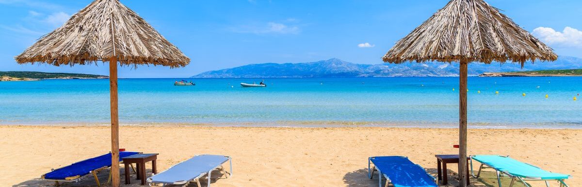 Umbrellas with sun beds on beautiful sandy Santa Maria beach with turquoise sea water, Paros island, Greece.