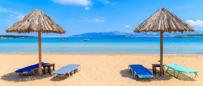 Umbrellas with sun beds on beautiful sandy Santa Maria beach with turquoise sea water, Paros island, Greece.