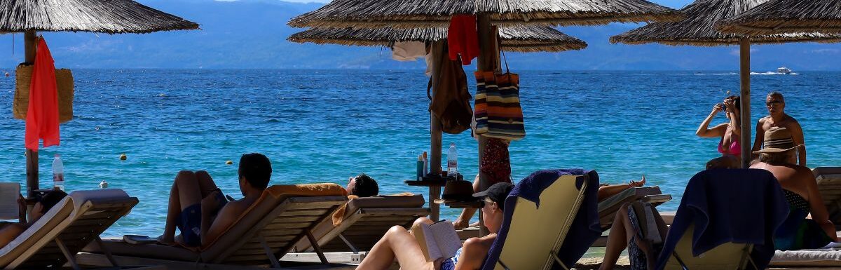 A view on a sand beach with straw parasols on a very warm and sunny summer day in Skiathos, Greece.