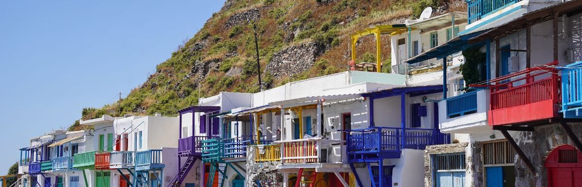 A beautiful view of colorful fishing houses by the sea under a green hill in Klima, Milos, Greece.