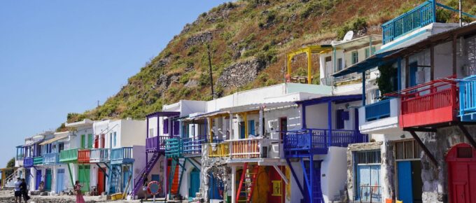 A beautiful view of colorful fishing houses by the sea under a green hill in Klima, Milos, Greece.