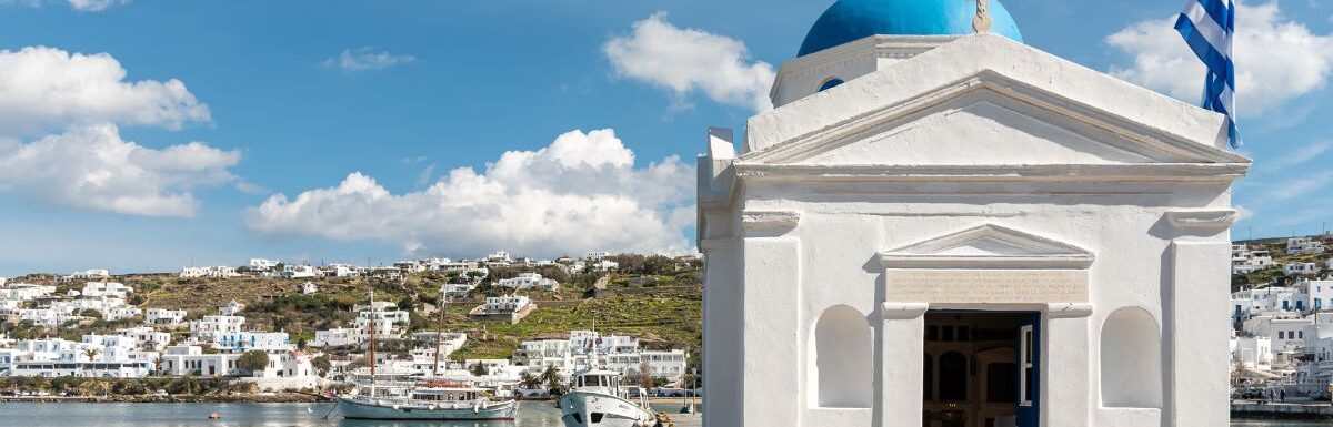 Greek church building and Greek flag in Old Port of Mykonos City, Mykonos, Greece.