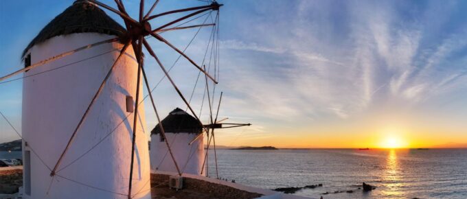 Panorama of traditional Greek windmills on Mykonos island at sunset with dramatic sky and Little Venice quarter with the tourist crowd in Mykonos, Greece in May.