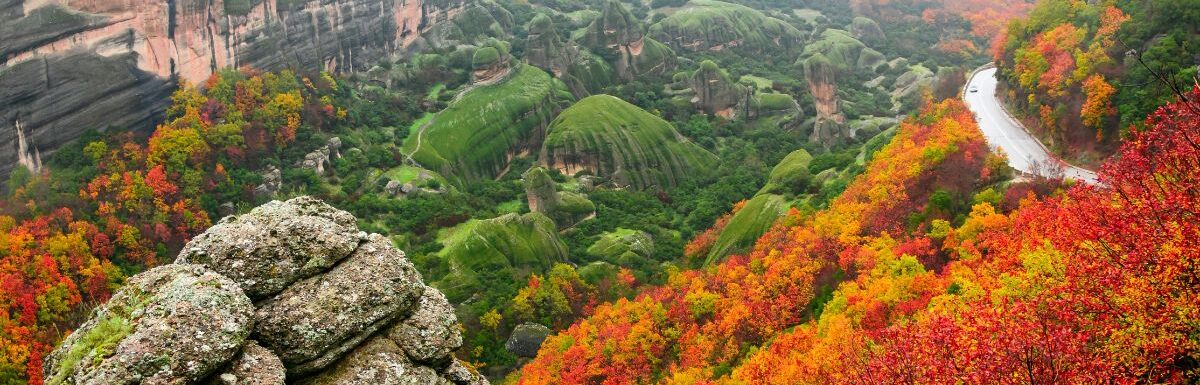 winding hillside road near the St. Barbara Roussanou Monastery during autumn, with fall colors on the leaves and fog covering the mountaintops in Meteora, Greece.