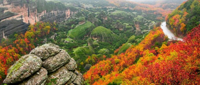 winding hillside road near the St. Barbara Roussanou Monastery during autumn, with fall colors on the leaves and fog covering the mountaintops in Meteora, Greece.