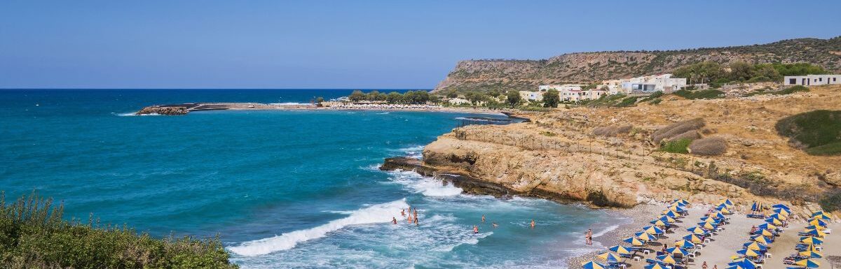 Bay with a sandy beach with umbrellas and people bathing in a tourist resort on the island of Crete, Greece.