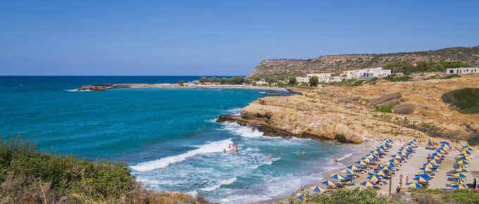 Bay with a sandy beach with umbrellas and people bathing in a tourist resort on the island of Crete, Greece.